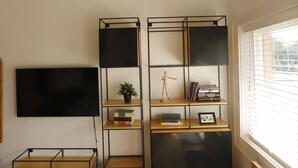 A room with a wooden ceiling, a black TV on the wall, a black bookshelf, and a window with blinds. - The Vine on main  (Stamford)
