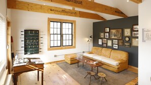 A cozy living room with a sofa, coffee table, and a foosball table. There are framed pictures on the wall and a window with blinds. - The Vine on main  (Stamford)