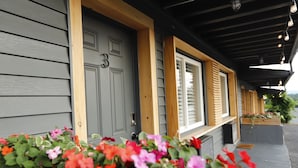 A building with a gray door marked with the number 3, wooden window frames, and a porch with potted plants. - The Vine on main  (Stamford)