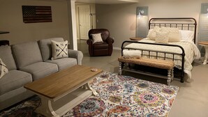 Um quarto com cama, sofá, poltrona, mesa pequena e tapete estampado.