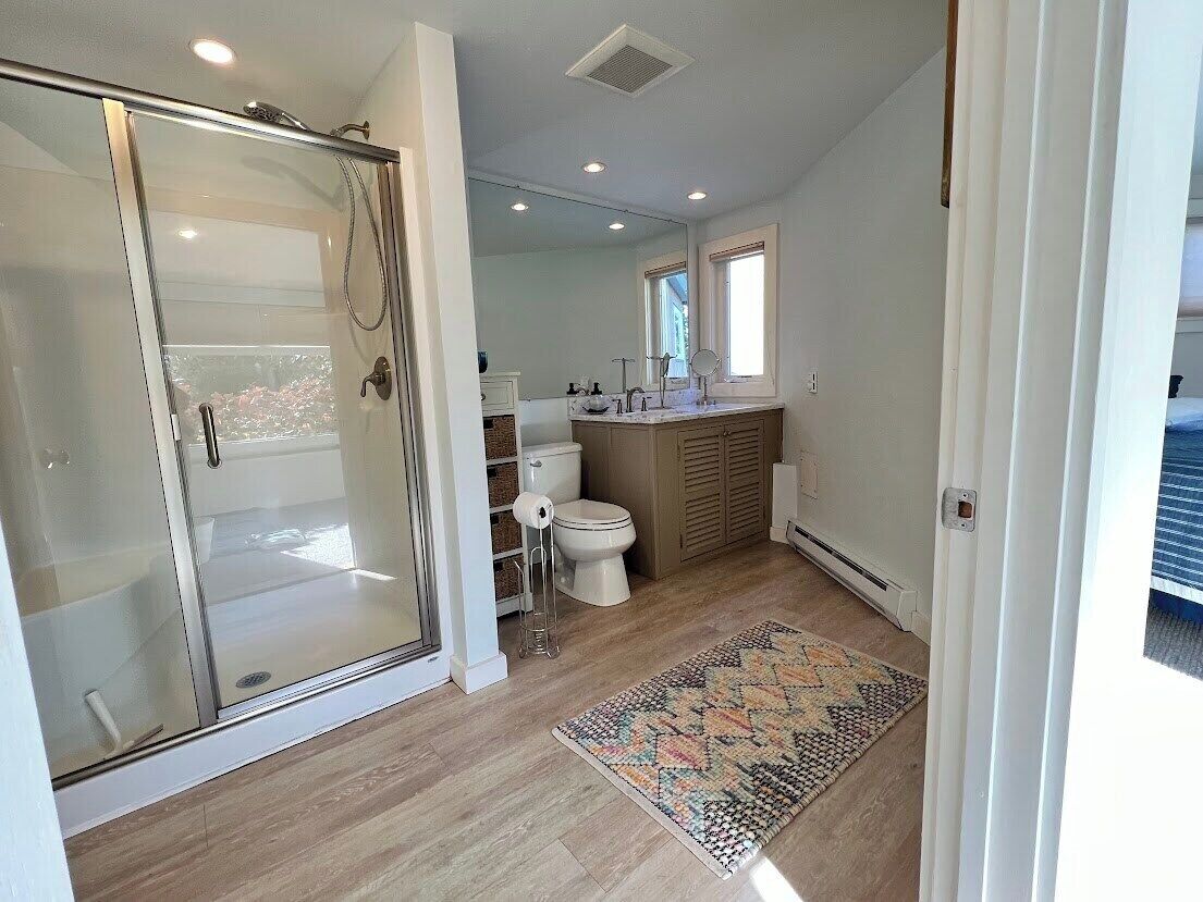 A bathroom with a glass shower enclosure, a toilet, and a sink area.