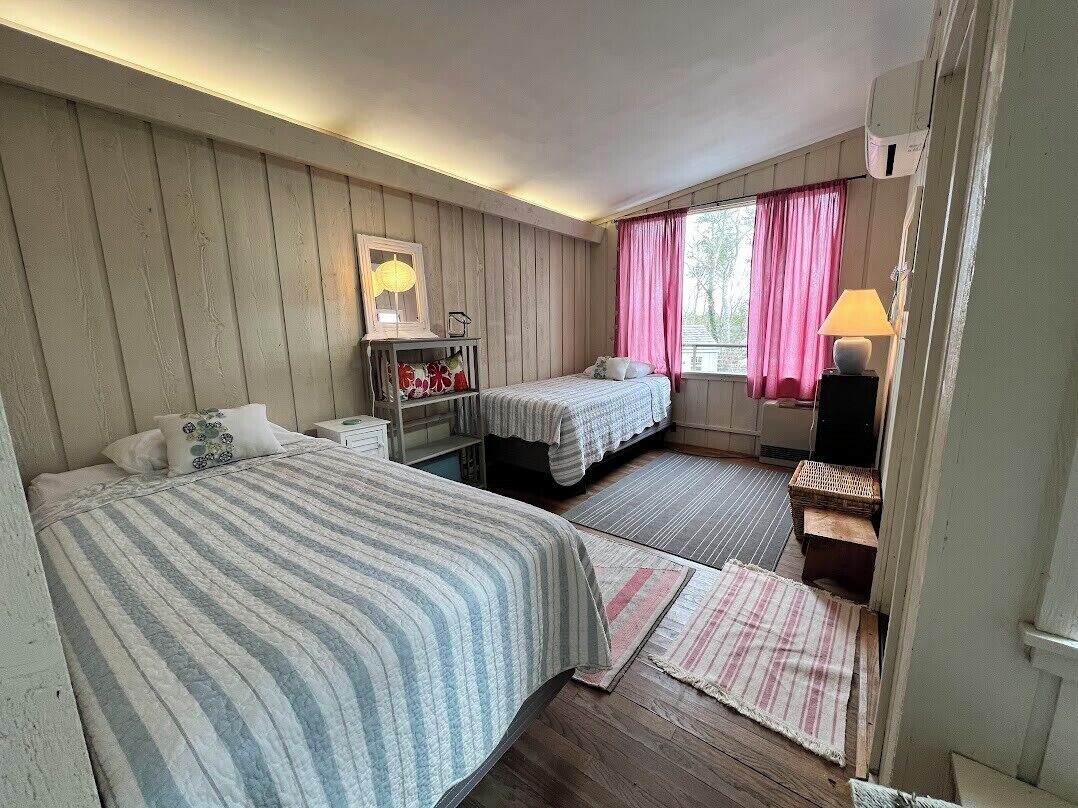 A room with two beds, a desk, a lamp, and a window with curtains.