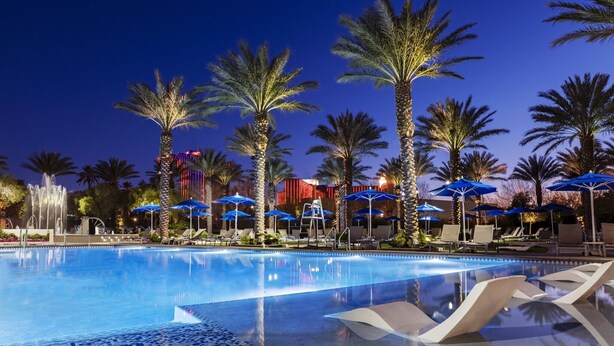 A pool area with lounge chairs and umbrellas, palm trees, and a fountain. - 3BD/Vegas Oasis w/Pool, Full Kitchen, and more! (Las Vegas)