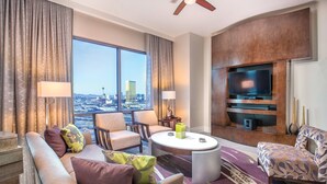 A modern hotel room with a large window offering a city view, a flat-screen TV mounted on a wooden wall, and a seating area with a round coffee table. - 3BD/Vegas Oasis w/Pool, Full Kitchen, and more! (Las Vegas)