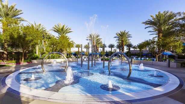 A circular water feature with multiple fountains, surrounded by palm trees and a pool area. - 3BD/Vegas Oasis w/Pool, Full Kitchen, and more! (Las Vegas)