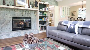 A living room with a stone fireplace, a leather sofa, a bookshelf, and a dining area with a chandelier.