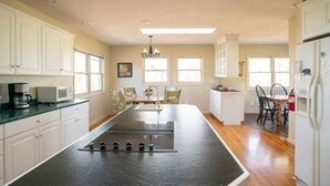 A kitchen with white cabinets, a central island with a stovetop, and a dining area with chairs and a table.