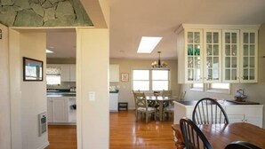 A spacious kitchen with white cabinets, a dining area with a wooden table and chairs, and a large window providing natural light.