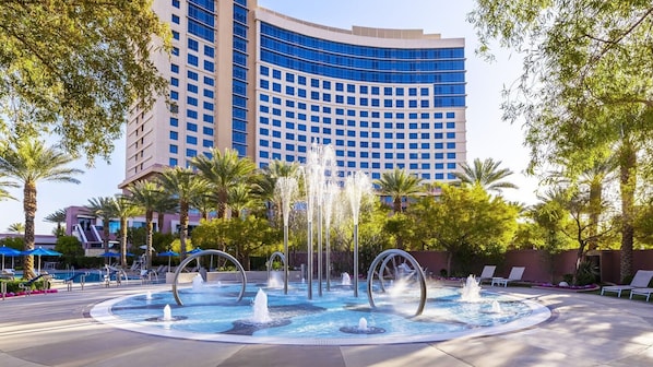 A hotel courtyard with a fountain, palm trees, and a large building in the background.