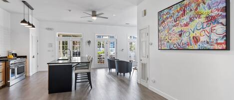 A spacious kitchen with modern appliances, a dining area with a central island, and a large abstract painting on the wall.