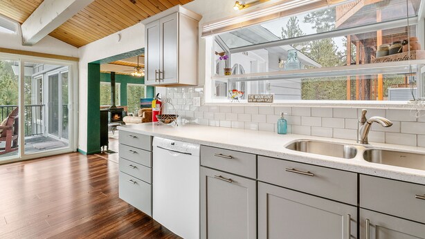 Una cocina moderna con armarios blancos, un lavamanos de acero inoxidable y una ventana con vistas a una terraza.