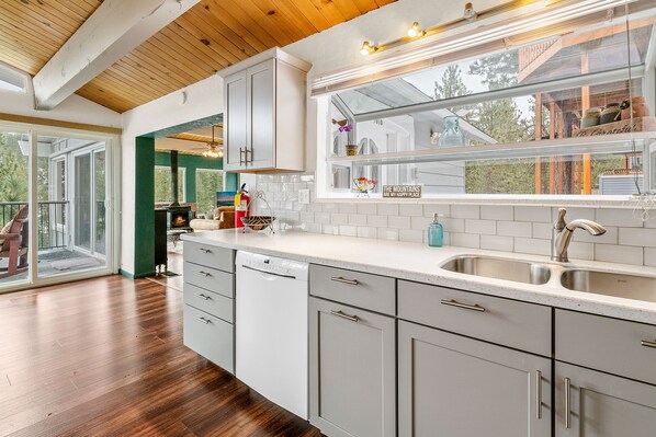 A modern kitchen with white cabinets, a stainless steel sink, and a window overlooking a deck.
