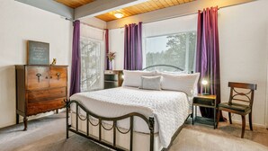 Un dormitorio con cama, cómoda de madera, mesita de noche, silla y una ventana con cortinas.