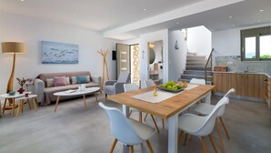 Una sala de estar moderna con una mesa de comedor de madera, sillas blancas, un sofá y un cuadro de gaviotas.
