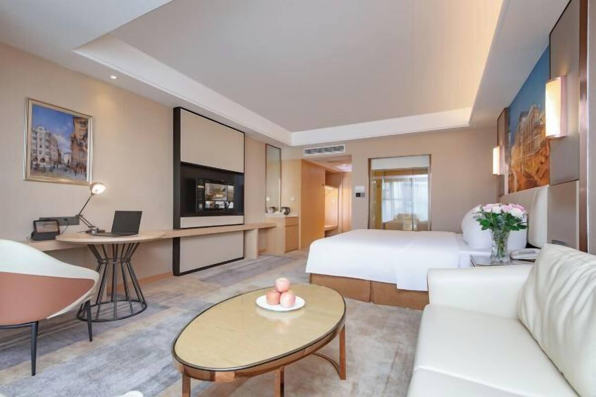 Ein modernes Hotelzimmer mit Bett, Schreibtisch mit Laptop, rundem Couchtisch und einer Couch.