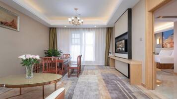 Una habitación de hotel con zona de comedor, televisión y un ventanal grande.