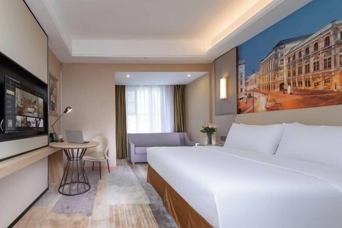 Ein Hotelzimmer mit einem Bett, einem Schreibtisch mit Stuhl, einem kleinen Tisch, einer Couch und einem Bild an der Wand.