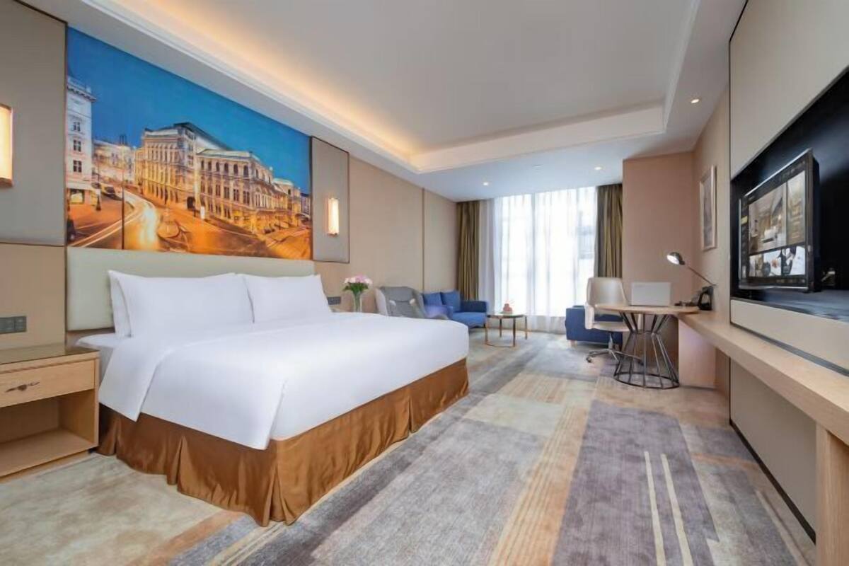 Ein Hotelzimmer mit einem großen Bett, einem Schreibtisch, einem Sessel, einem Fernseher und einem Stadtbild.