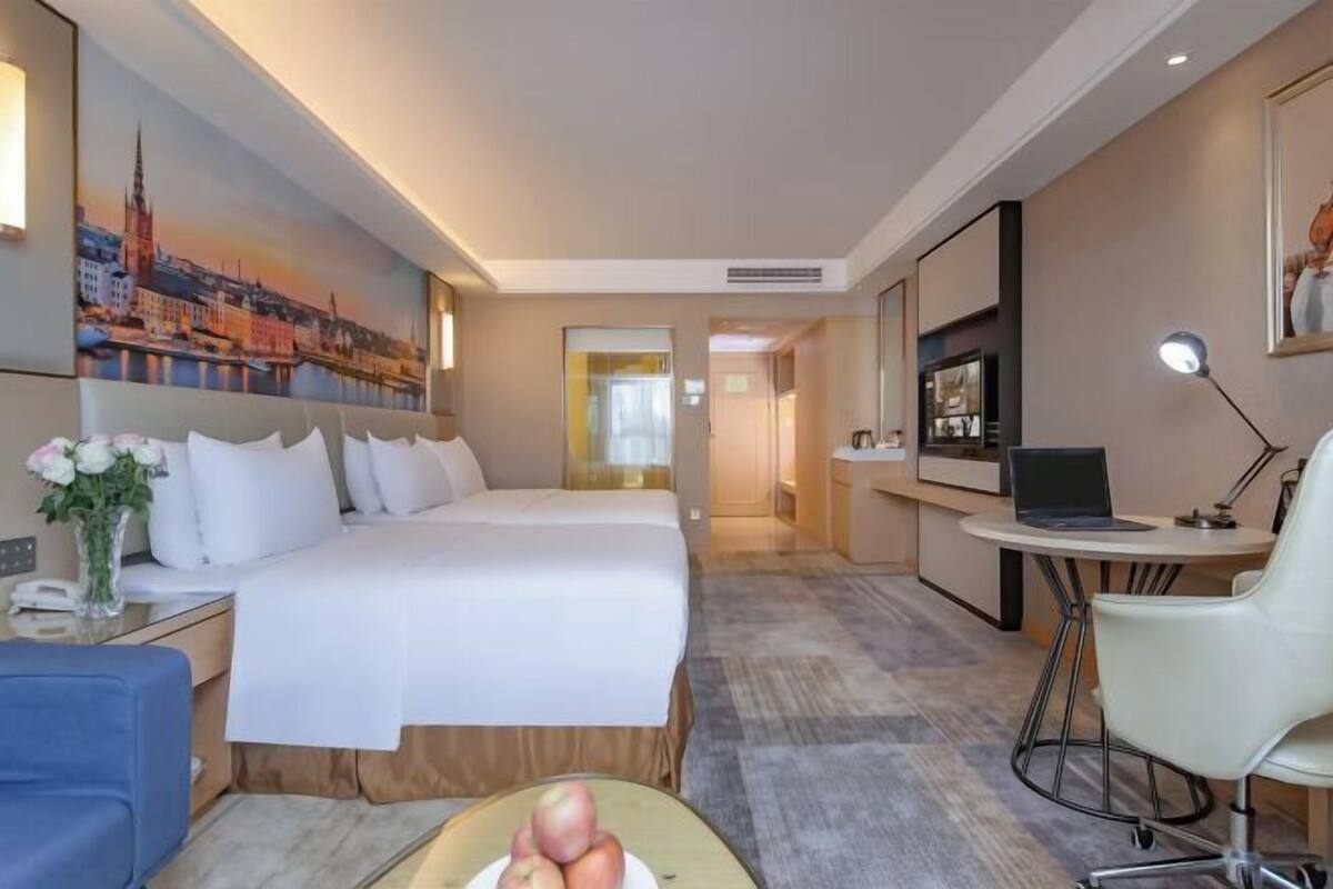 Ein Hotelzimmer mit Bett, Schreibtisch, Laptop, Stuhl und einem Stadtbild.