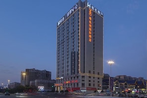 Un grand hôtel à plusieurs étages, avec une enseigne bien visible sur le côté, situé sur une rue animée au premier plan.