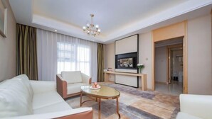 Een moderne hotelkamer met een bank, een salontafel, een televisie en een groot raam met gordijnen.