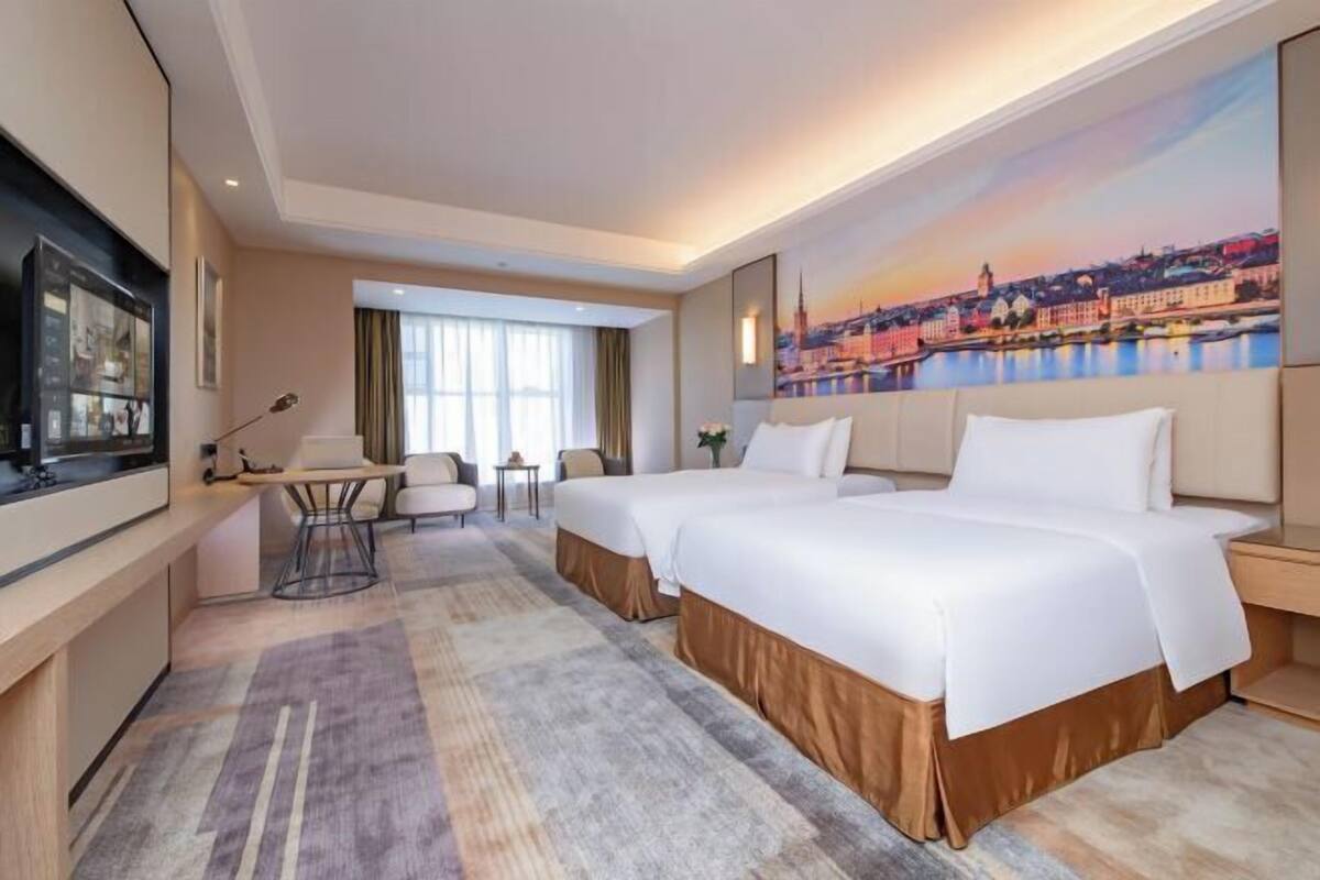 Ein Hotelzimmer mit zwei Betten, einem Fernseher, einem Schreibtisch und einem großen Fenster.