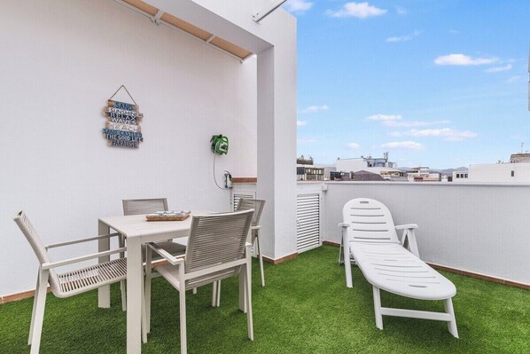 Terraço no telhado com mesa e cadeiras brancas, uma poltrona de descanso e um letreiro fixado na parede.