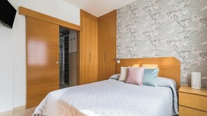A bedroom with a bed, wooden wardrobe, and a wall with a floral pattern.