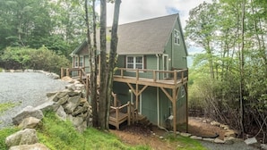 Eine Holzhütte mit einer Holzterrasse, umgeben von Bäumen und einer felsigen Küstenlinie.