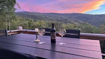 A table with two wine glasses and a bottle, set against a scenic view of a forested mountain range.