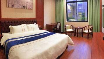 A hotel room with a large bed, a desk, two chairs, and a window with curtains.