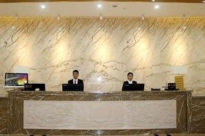 Un comptoir d’accueil avec deux employés, un mur en marbre orné d’un motif et un écran numérique.