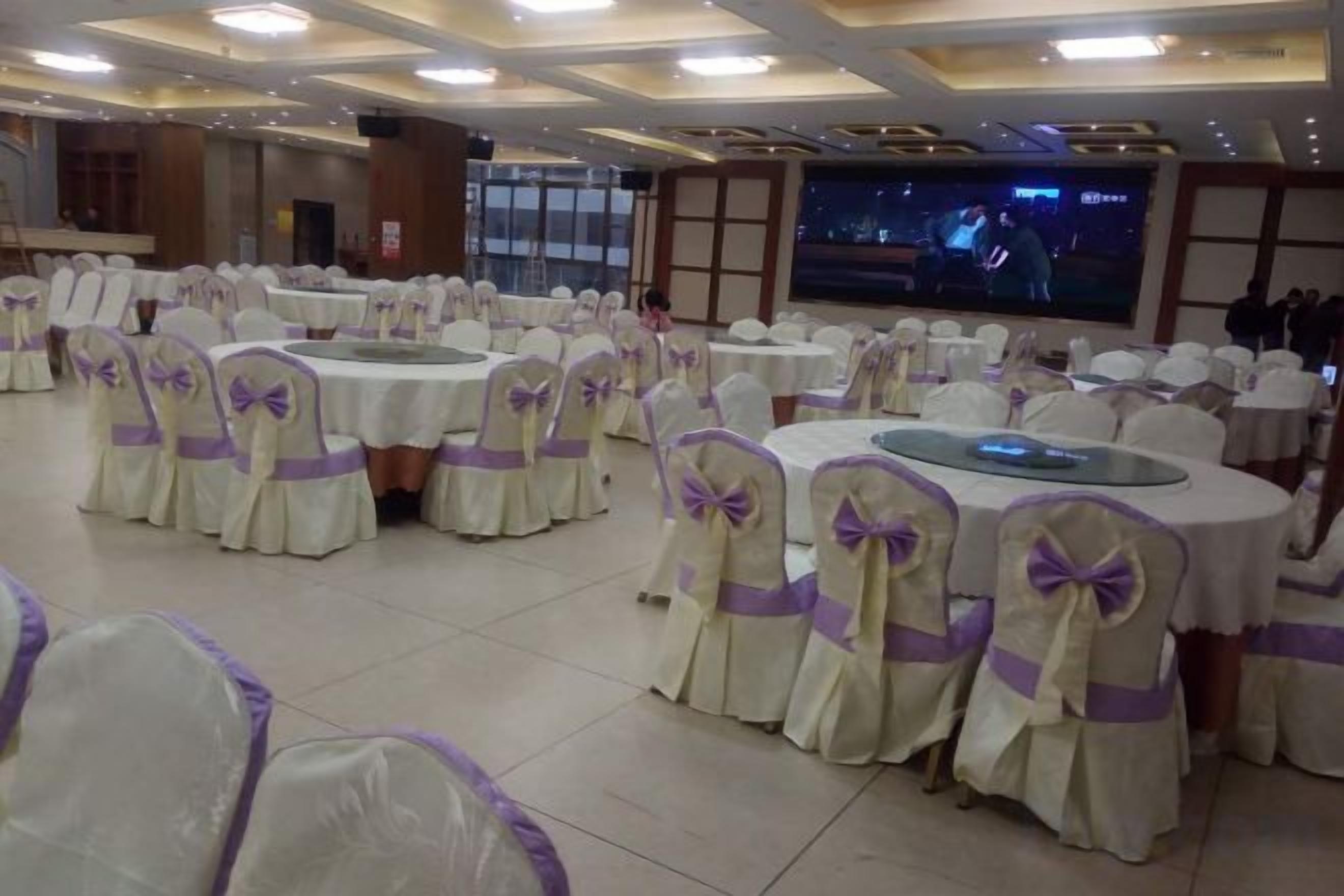 A banquet hall with round tables, chairs with bow ties, and a large screen.