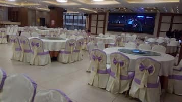 A banquet hall with round tables, chairs with bow ties, and a large screen.
