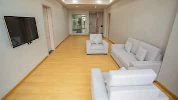 A spacious living area with a flat-screen TV mounted on the wall, a white sofa, and a matching ottoman.