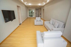 A spacious living area with a flat-screen TV mounted on the wall, a white sofa, and a matching ottoman. - Maomingjia International Hotel (Dianbai Wanda Plaza Branch) (Maoming)