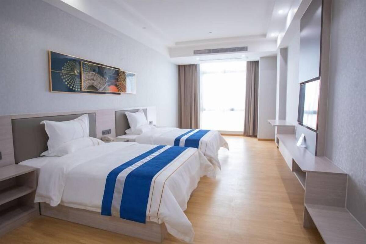 Habitación de hotel con dos camas, televisión, un cuadro en la pared y ventana con cortinas.