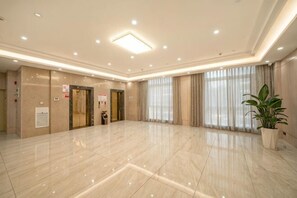 Un vestíbulo amplio con piso de mármol, dos ascensores y una planta en maceta.
