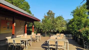 An outdoor seating area with tables and chairs, a building with signage, and trees in the background.