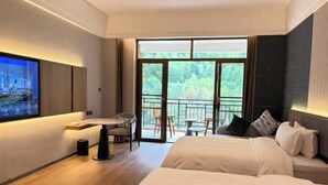 A hotel room with a large bed, a desk with a chair, a TV, and a balcony with a view of trees. - Wugong Mountain Rongyuan International Hot Spring Resort (Anfu)