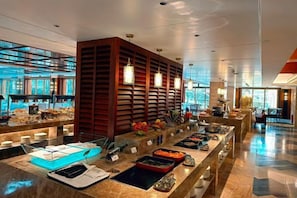Un bufé moderno en un hotel, con diversas opciones de comida, una zona de estar y un amplio ventanal con vistas al exterior.