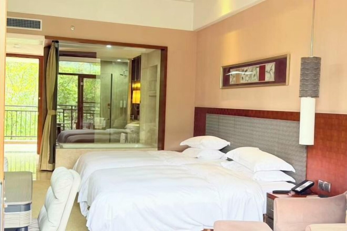 A hotel room with a large bed, a bedside table, a chair, and a glass door leading to a balcony.