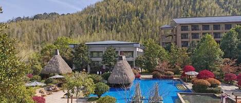 A resort with a swimming pool, thatched-roof structures, and a mountain backdrop.