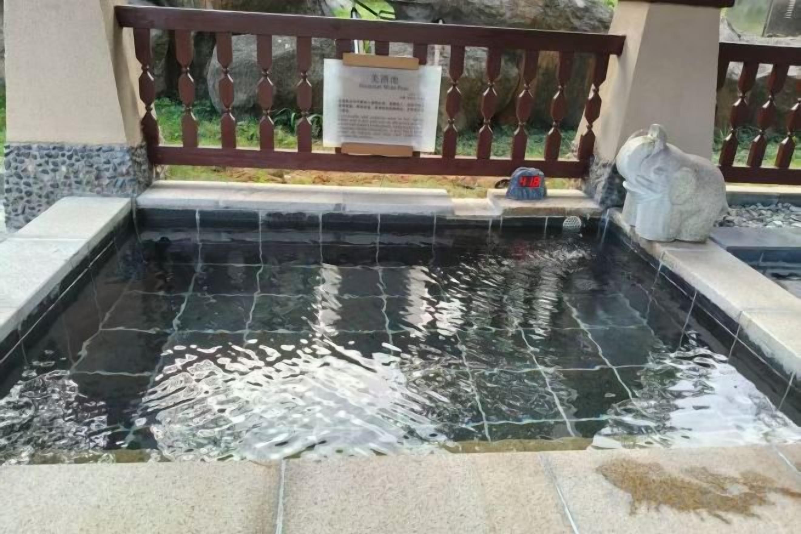 Ein rechteckiger Pool mit einer gefliesten Kante, einem Holzzaun und einer Steinstatue.