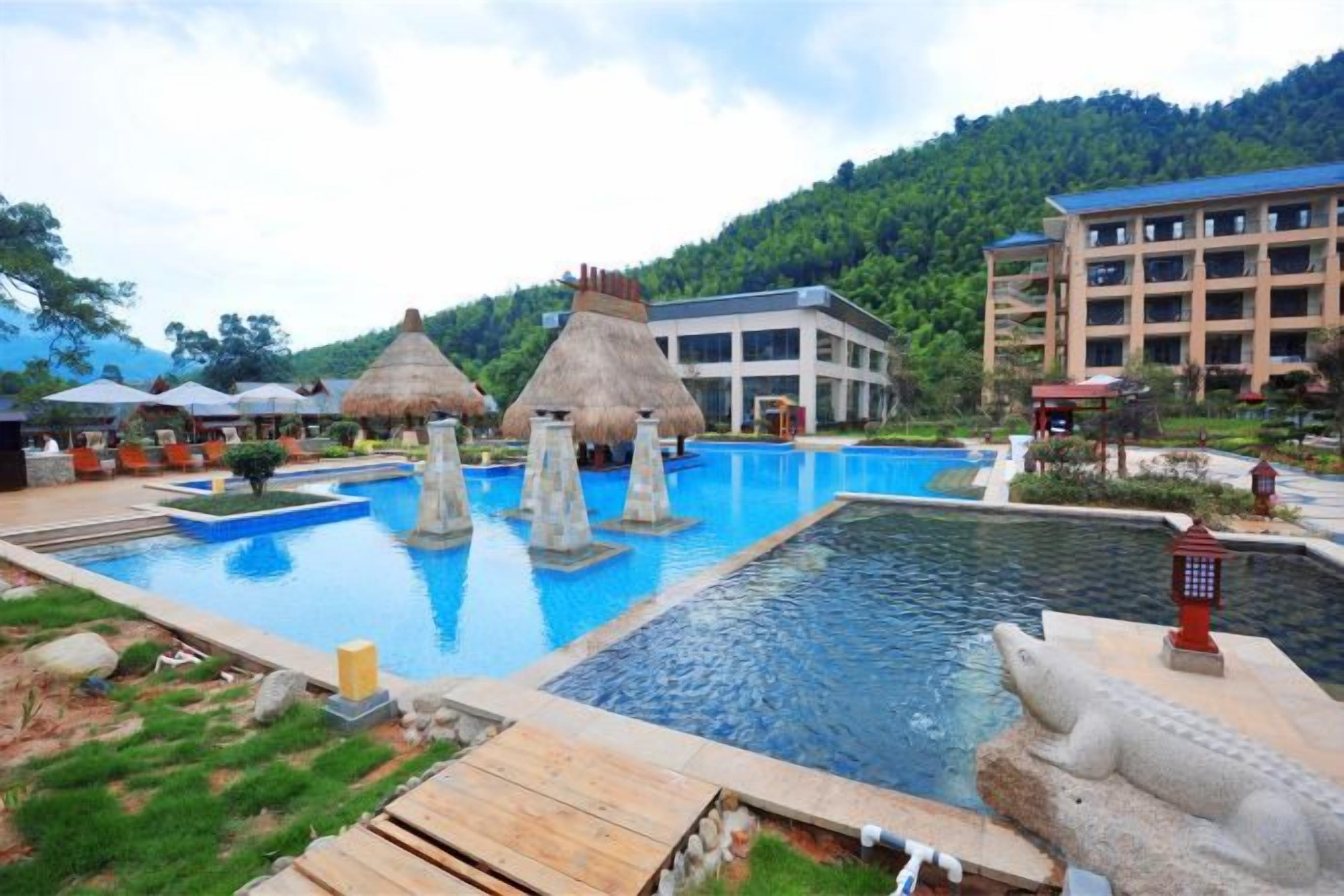 Una piscina con varias secciones, una estructura de techo de paja y un edificio grande al fondo.
