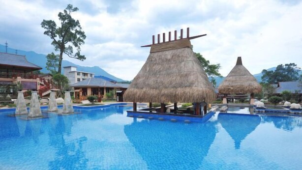 A swimming pool with thatched-roof structures, surrounded by buildings and mountains. - Wugong Mountain Rongyuan International Hot Spring Resort (Anfu)
