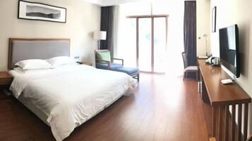 A hotel room with a large bed, a desk with a TV, a chair, and a window with curtains.