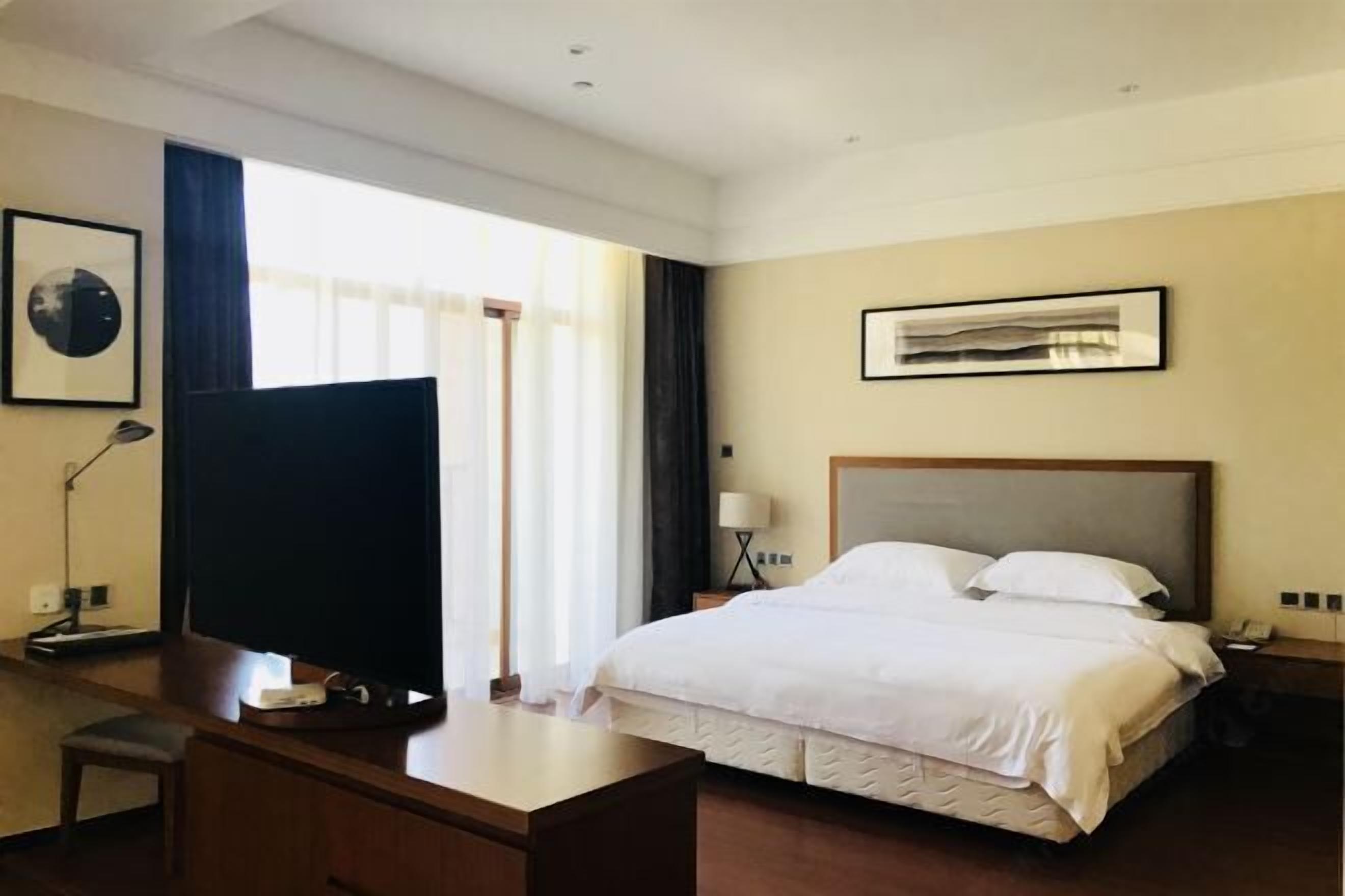 A hotel room with a large bed, a desk, a television, and a window with curtains.