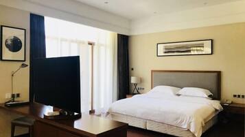 A hotel room with a large bed, a desk, a television, and a window with curtains.
