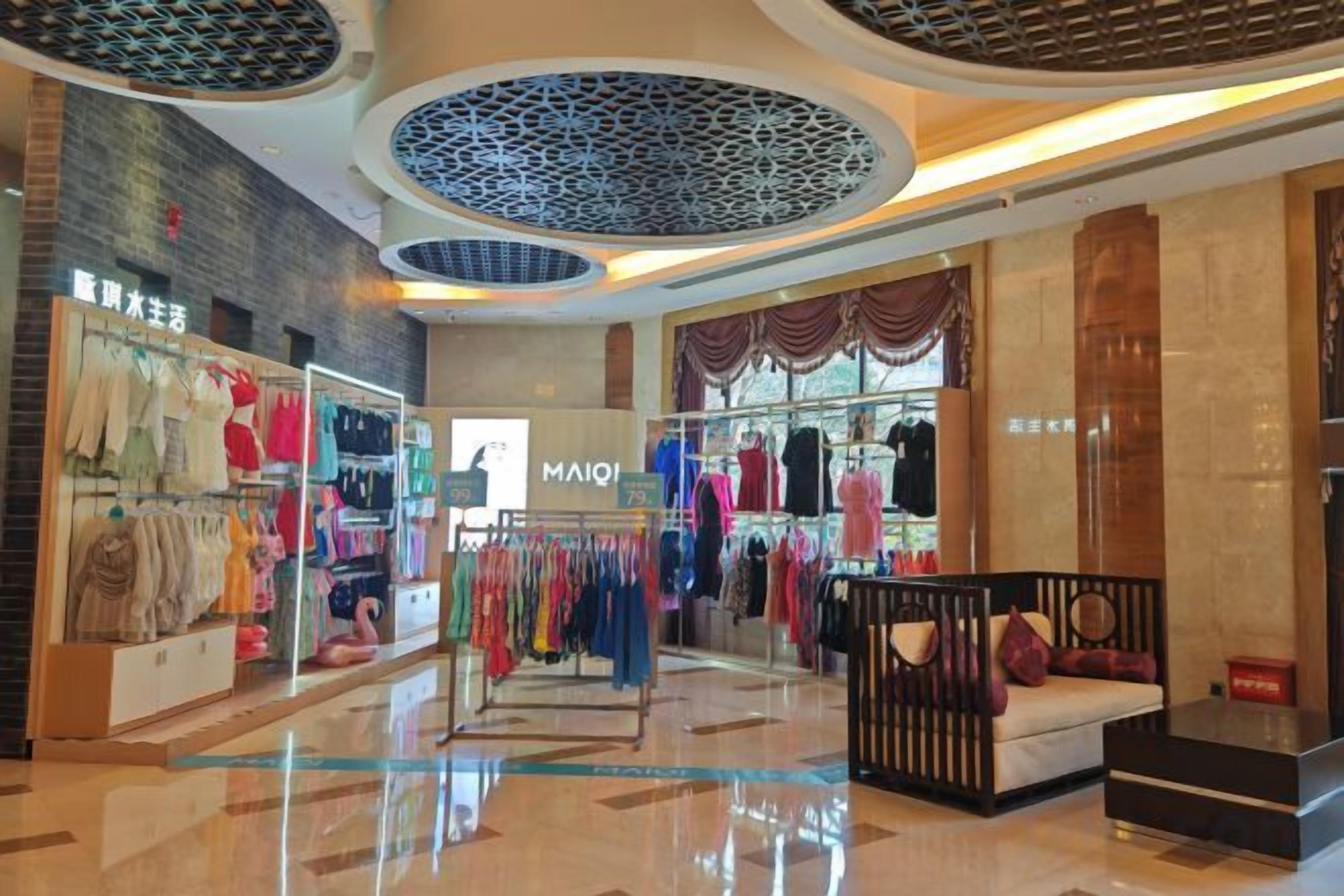 Interior de un centro comercial con tiendas de ropa, una zona de estar y un techo decorativo.
